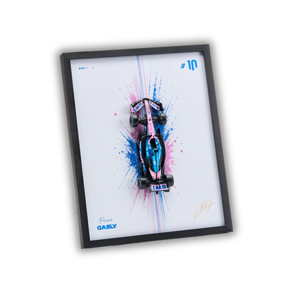 A framed art print featuring a pink and blue Formula 1 race car on a white background with paint splatters, signed by Jean Alesi. The print is housed in a black frame and shown at an angle on a plain white background.