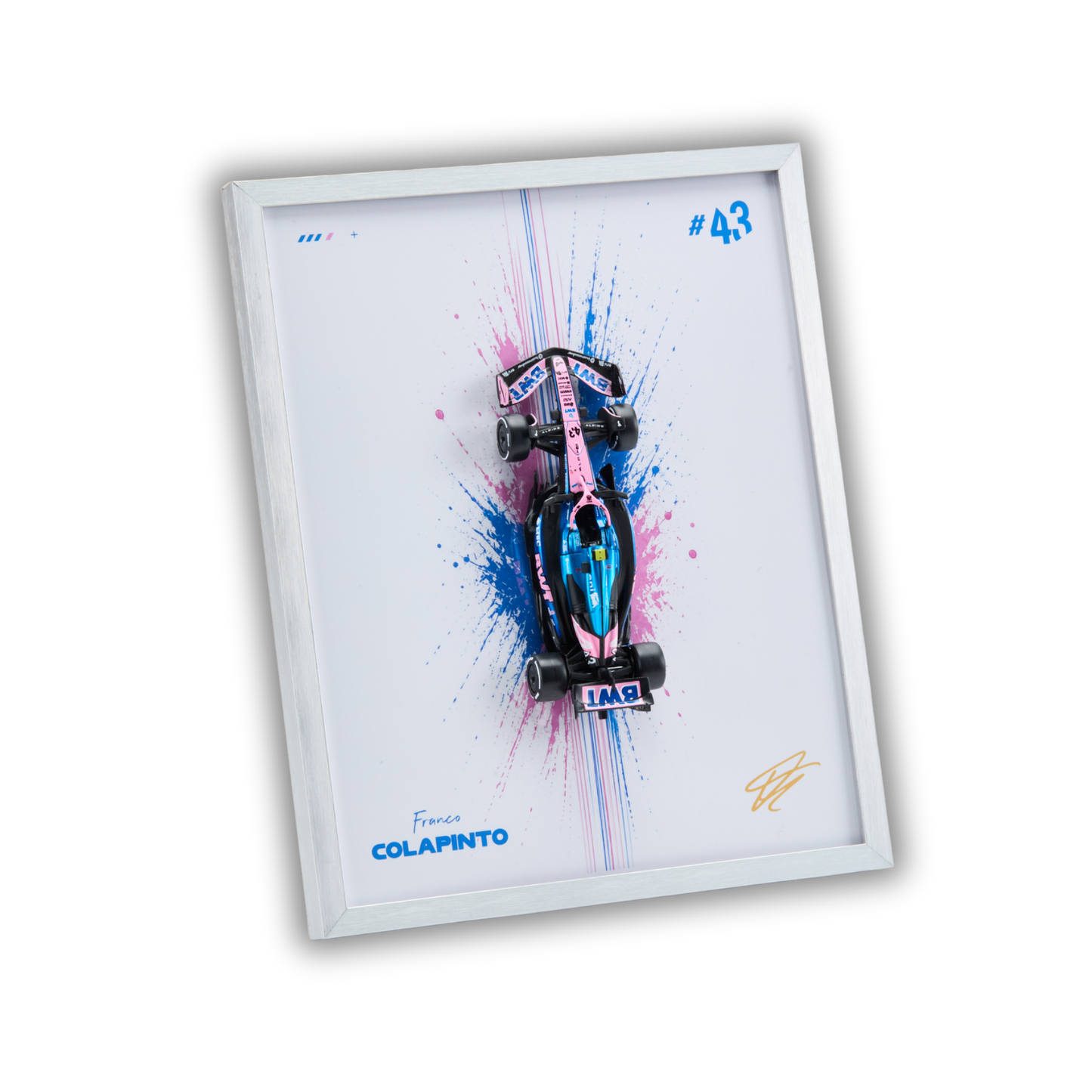 A framed wall art print featuring a stylized Formula 1 car in pink, blue, and black over a white background with paint splatter, shown at an angle on a black backdrop.