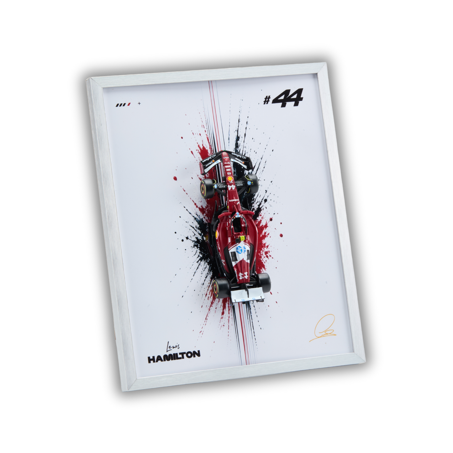 A framed art print featuring a red Formula 1 race car on a white background with black paint splatters, the number 44, and signatures including Hamilton's name and a gold signature. The frame is shown at an angle against a plain white background.