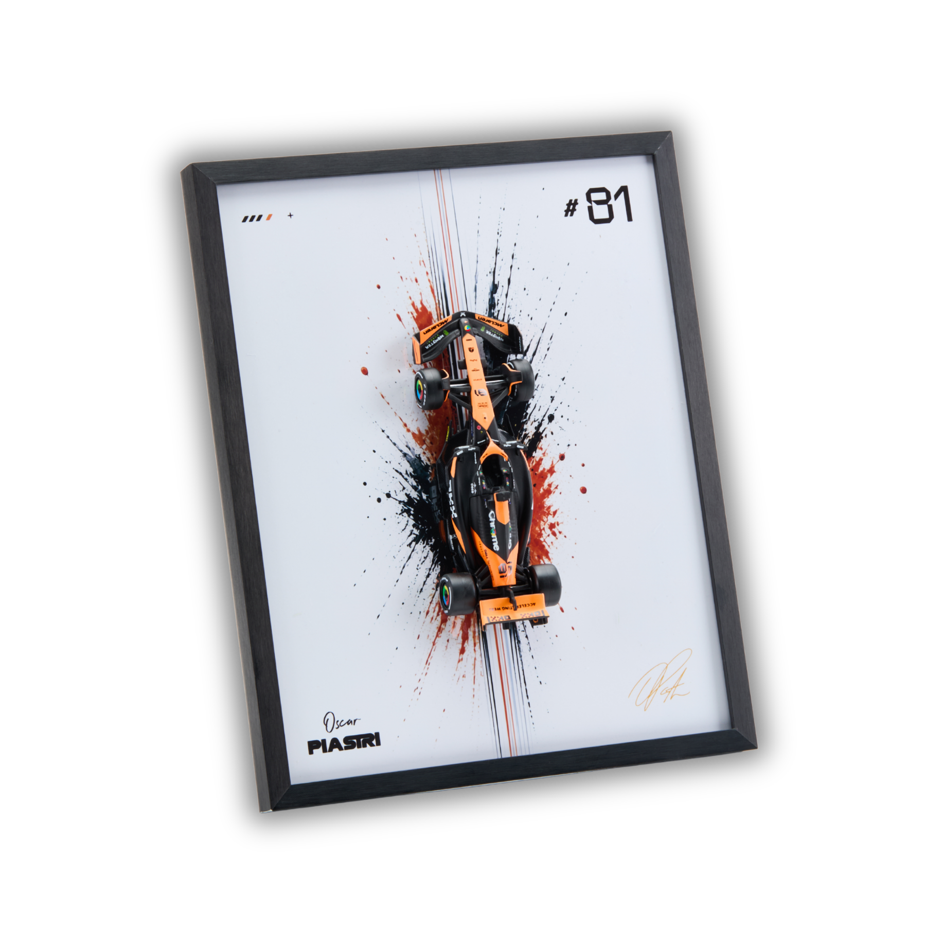 A framed art print featuring an orange and black Formula 1 car on a white background with paint splatters, presented in a black frame against a white background.